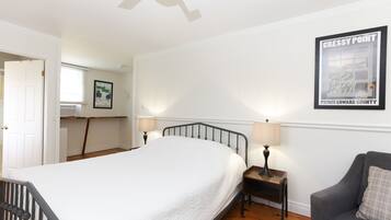 A bedroom with a large bed, two bedside tables with lamps, a grey armchair, and a ceiling fan.