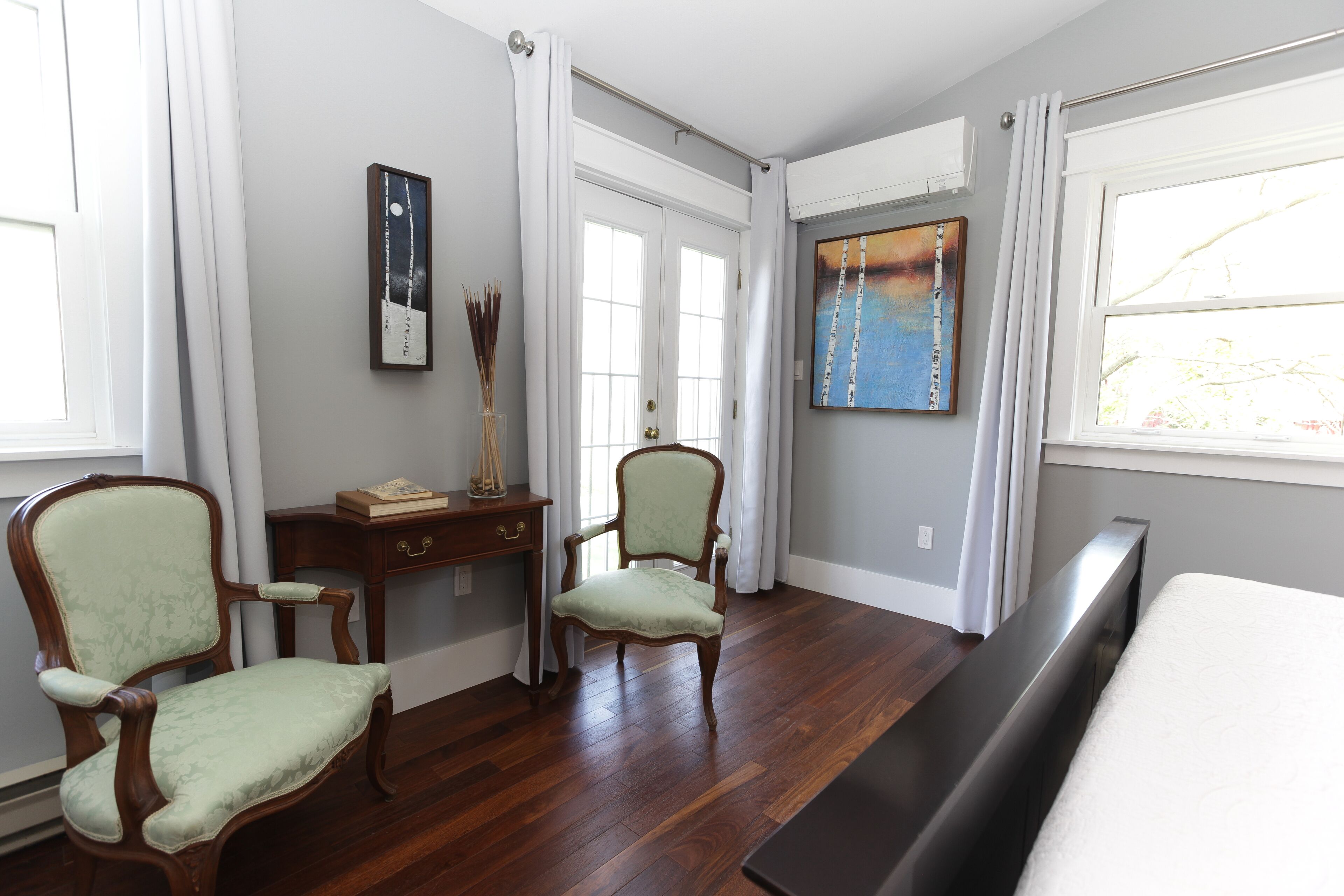 A room with a bed, two chairs, a desk, and a painting on the wall.