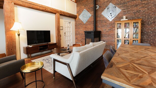 A living room with a brick wall, a fireplace, a sofa, a TV, and a wooden cabinet. - Jackson's Falls Country Inn (Prince Edward)