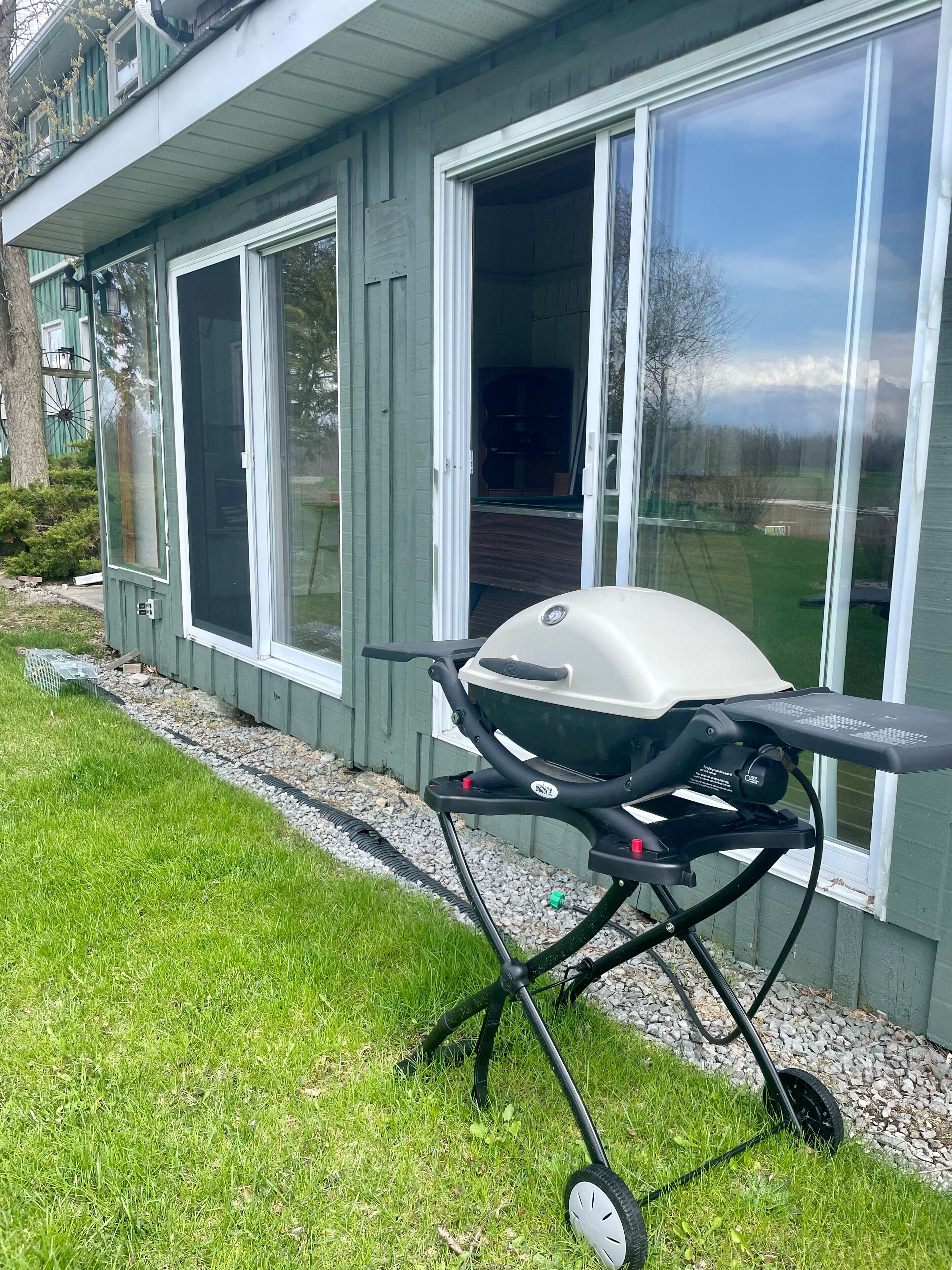 A portable grill set up in front of a house with sliding glass doors.