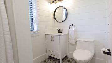 A bathroom with a white vanity, a toilet, a mirror, and a window with blinds.