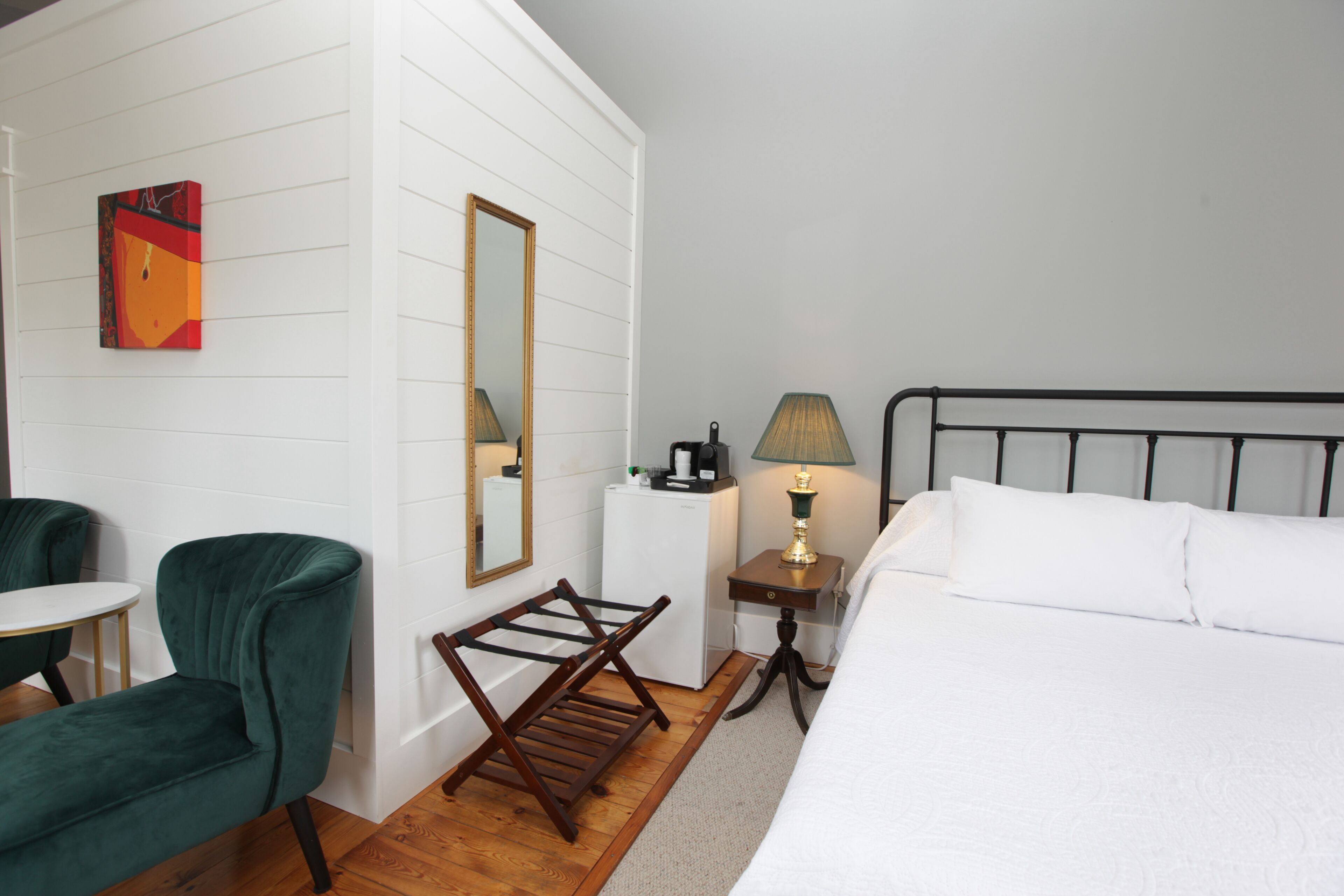 Une chambre d’hôtel avec un lit, une chaise, une petite table, une lampe et un miroir.
