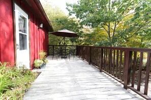 A wooden deck with a red building, outdoor furniture, and a view of trees. - Jackson's Falls Country Inn (Prince Edward)