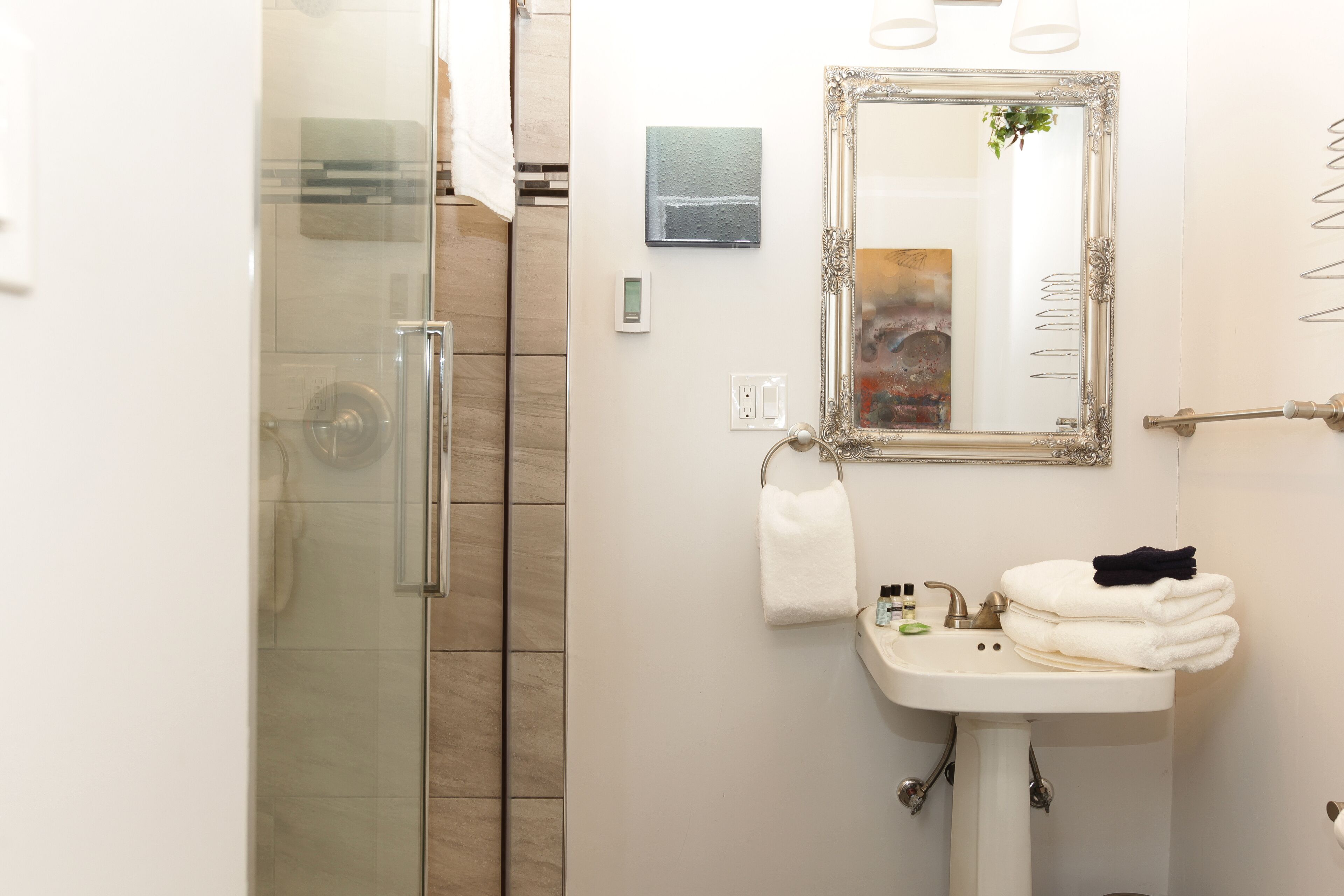 Ein Badezimmer mit Duschkabine aus Glas, Waschbecken mit Spiegel und Handtüchern.