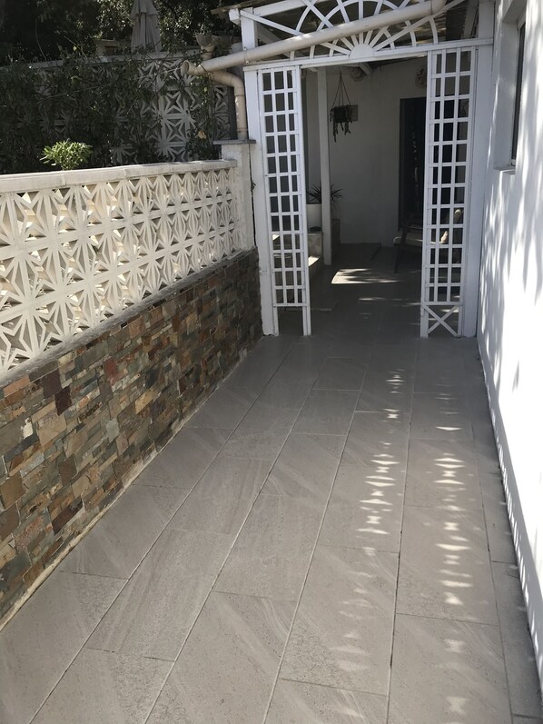 A covered outdoor area with a tiled floor, a brick wall, and a white decorative fence.