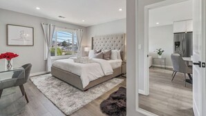 A modern bedroom with a large bed, a desk, and a view of the city. - Luxury 7BR Home Near SFO w/Parking (Daly City)