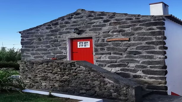 Ein Steinhaus mit roter Tür und kleinem Fenster.