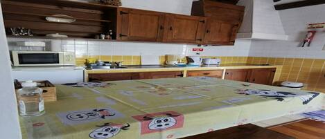 Une cuisine avec des meubles de rangement en bois, un four à micro-ondes et une table recouverte d’une nappe à motifs de dessins animés.