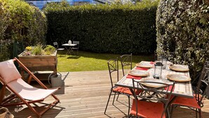 Una terraza de madera con una mesa lista para comer, rodeada de sillas y cojines.