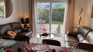 Un comedor con una mesa dispuesta para cuatro personas, un sofá, una lámpara y vistas a un jardín a través de un ventanal.