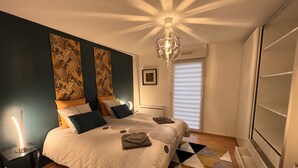 Un dormitorio con cama, una mesita de noche, una lámpara, un candelabro y una ventana con persianas.