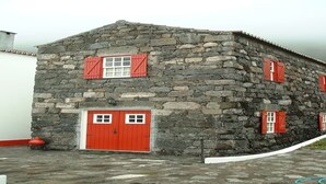 Ein Steinhaus mit roten Türen und Fensterläden, das einen schlichten, rustikalen Baustil aufweist.