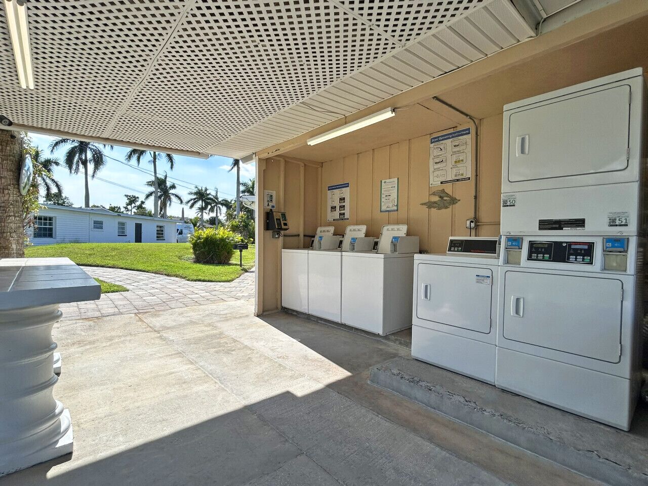A laundry facility with multiple washing machines and dryers, a tiled floor, and a covered area with a ceiling.