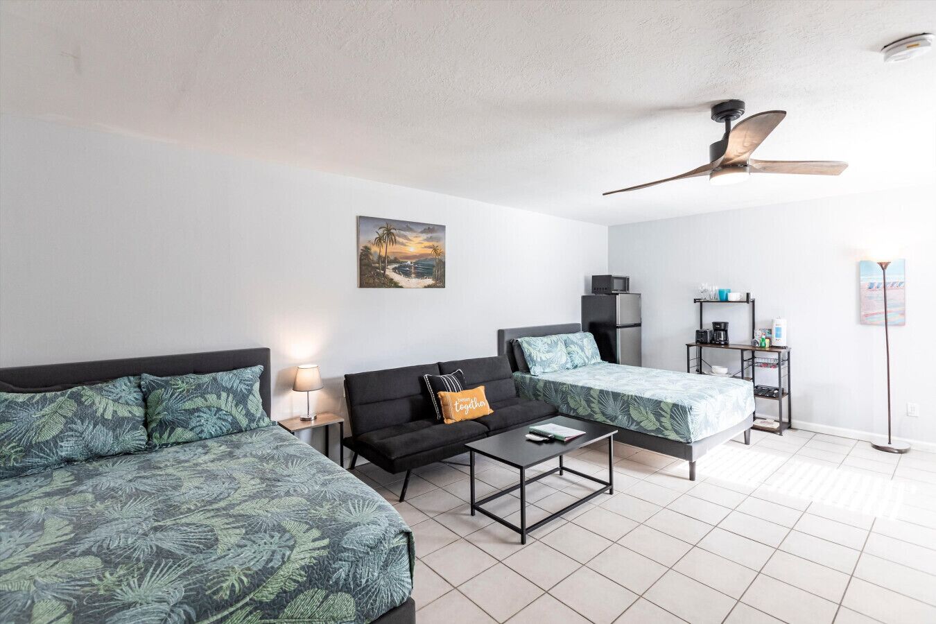 A modern hotel room with two beds, a sofa, a coffee table, a desk, and a ceiling fan.