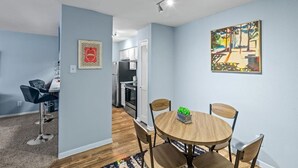 Eine moderne Küche mit Edelstahlgeräten, ein Essbereich mit einem runden Holztisch und vier Stühlen sowie ein Wohnbereich mit einer Couch und einem Couchtisch.