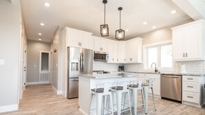A modern kitchen with white cabinets, stainless steel appliances, and a central island with bar stools. - Luxury Mountain Escape (Hendersonville)