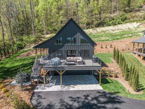 Une maison moderne à deux étages dotée d’une grande terrasse, entourée d’une pelouse bien entretenue et d’arbres.