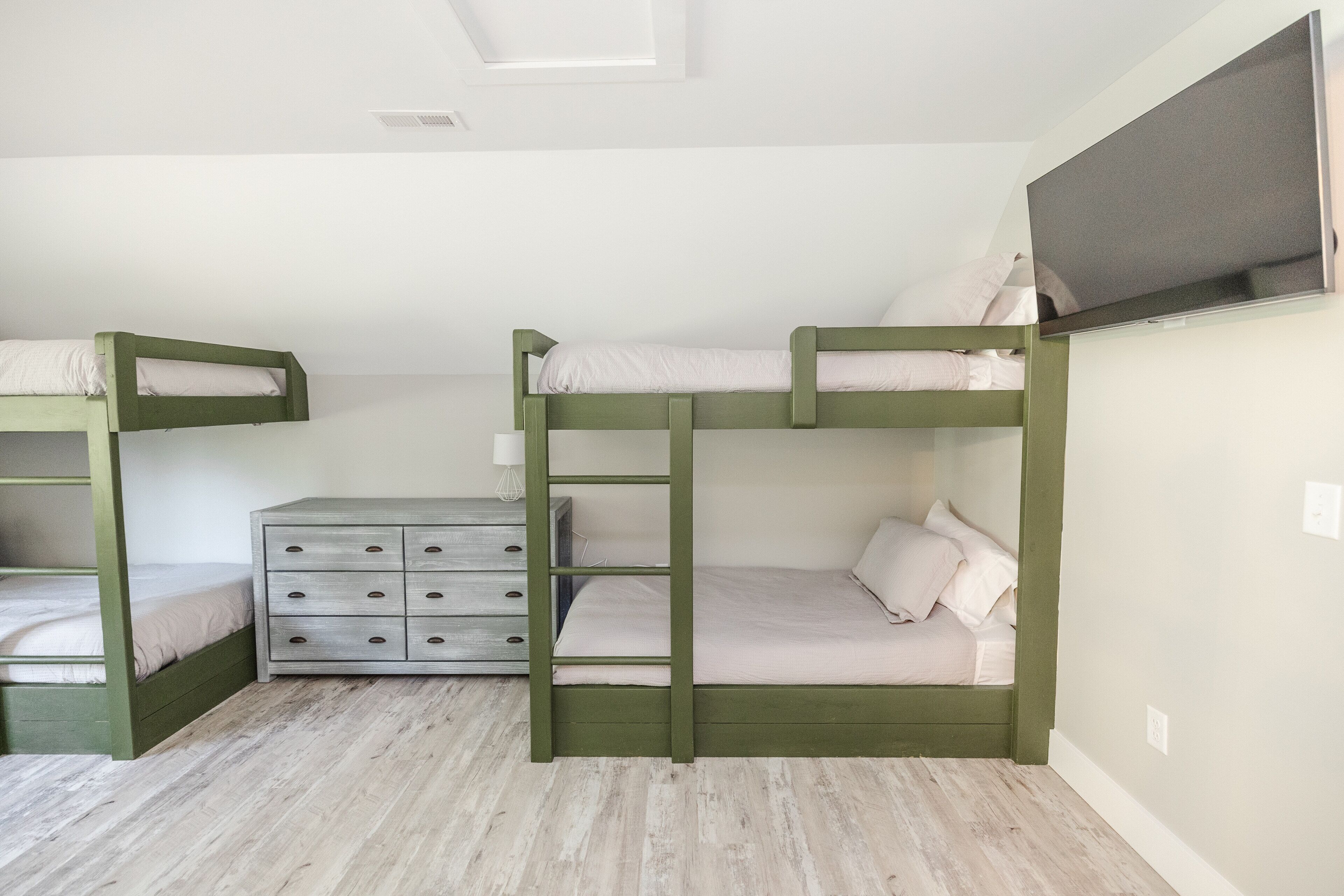 A bunk bed room with a dresser and a flat-screen TV.