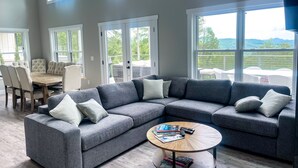A spacious living room with a grey sectional sofa, a round coffee table, and a dining area with a wooden table and chairs. - Luxury Mountain Escape (Hendersonville)