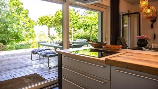 Eine moderne Küche mit großem Fenster, einer Holzterrasse und einer Sitzgelegenheit im Freien.