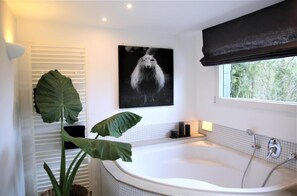 Un bagno moderno con una vasca da bagno ampia, un'opera d'arte in bianco e nero e una pianta di grandi dimensioni.