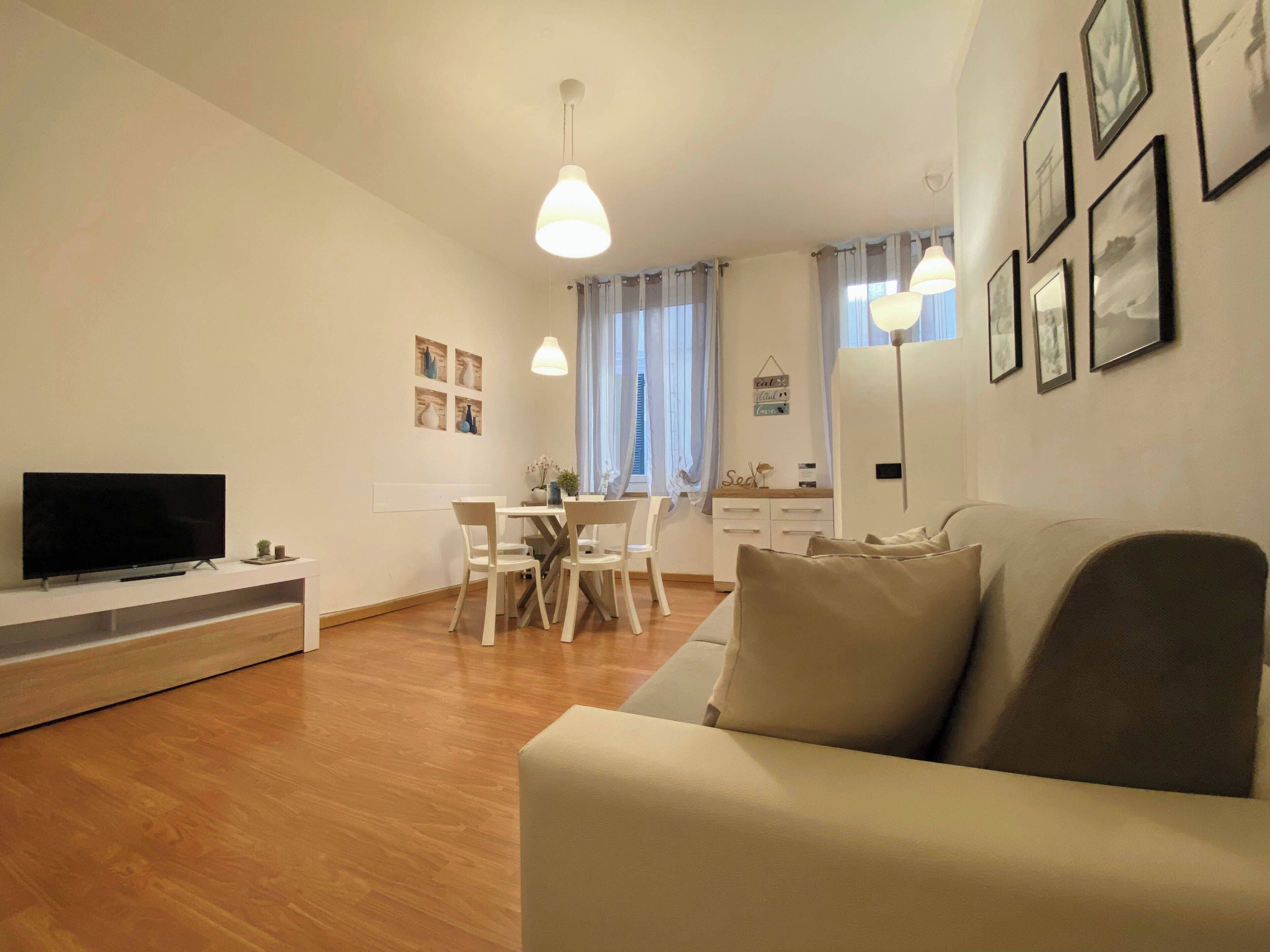Un soggiorno moderno con una TV a schermo piatto, un divano, un tavolo da pranzo con sedie e una zona cucina sullo sfondo.