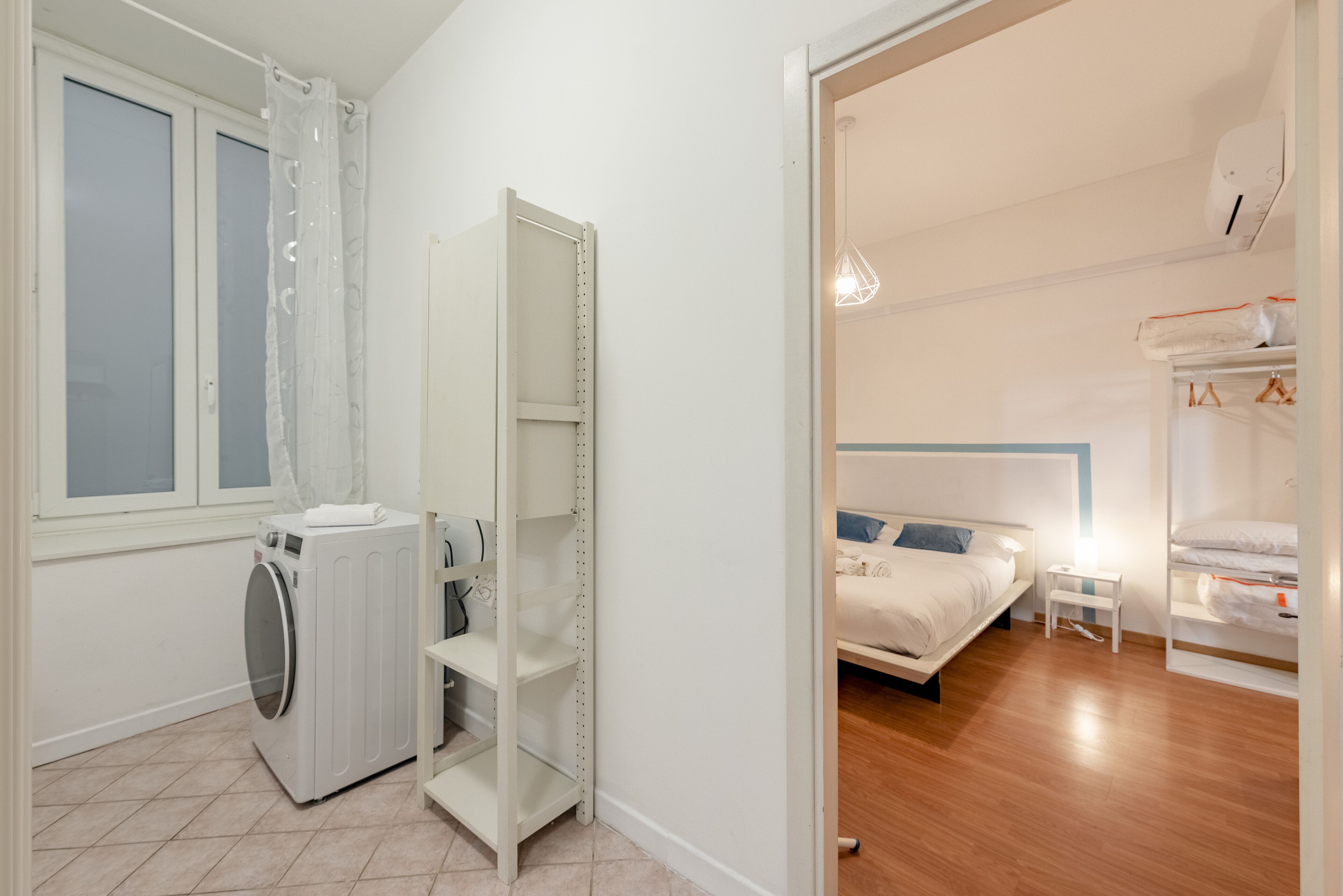 A modern bedroom with a bed, a nightstand, a wardrobe, and a built-in washing machine.