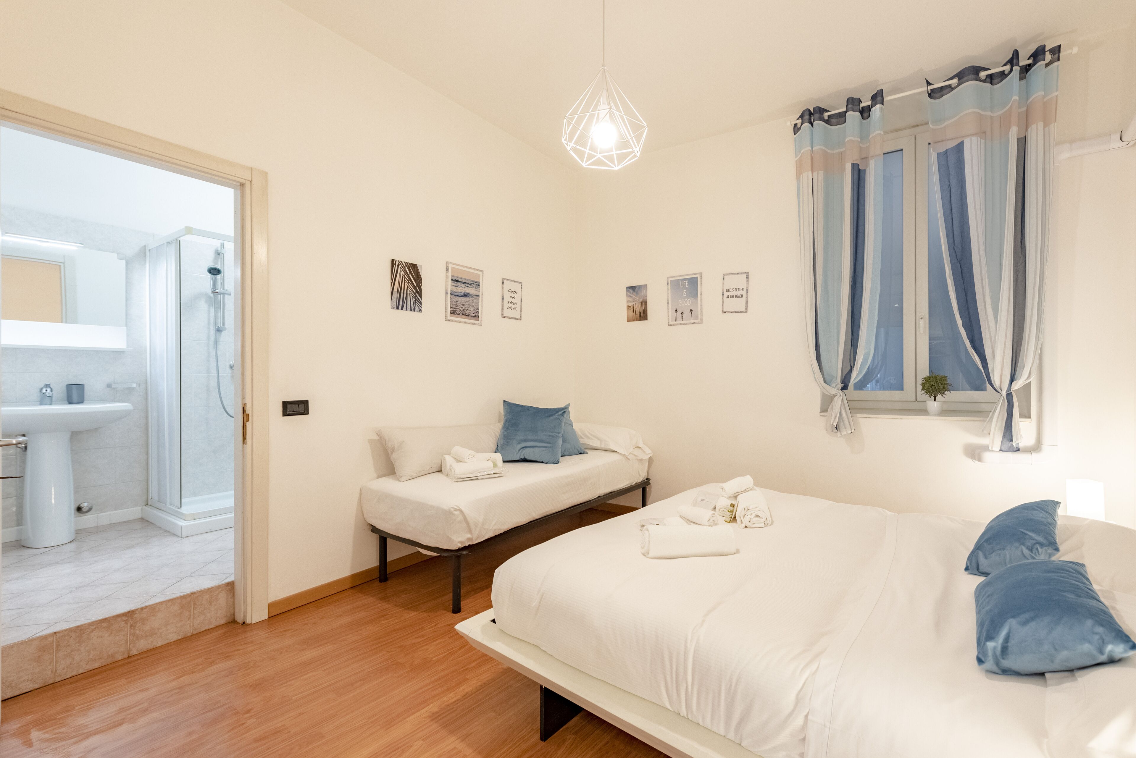 Une chambre à coucher comprenant un grand lit, un lit plus petit, une table de chevet, une commode, une fenêtre avec des rideaux et un luminaire fixé au mur.