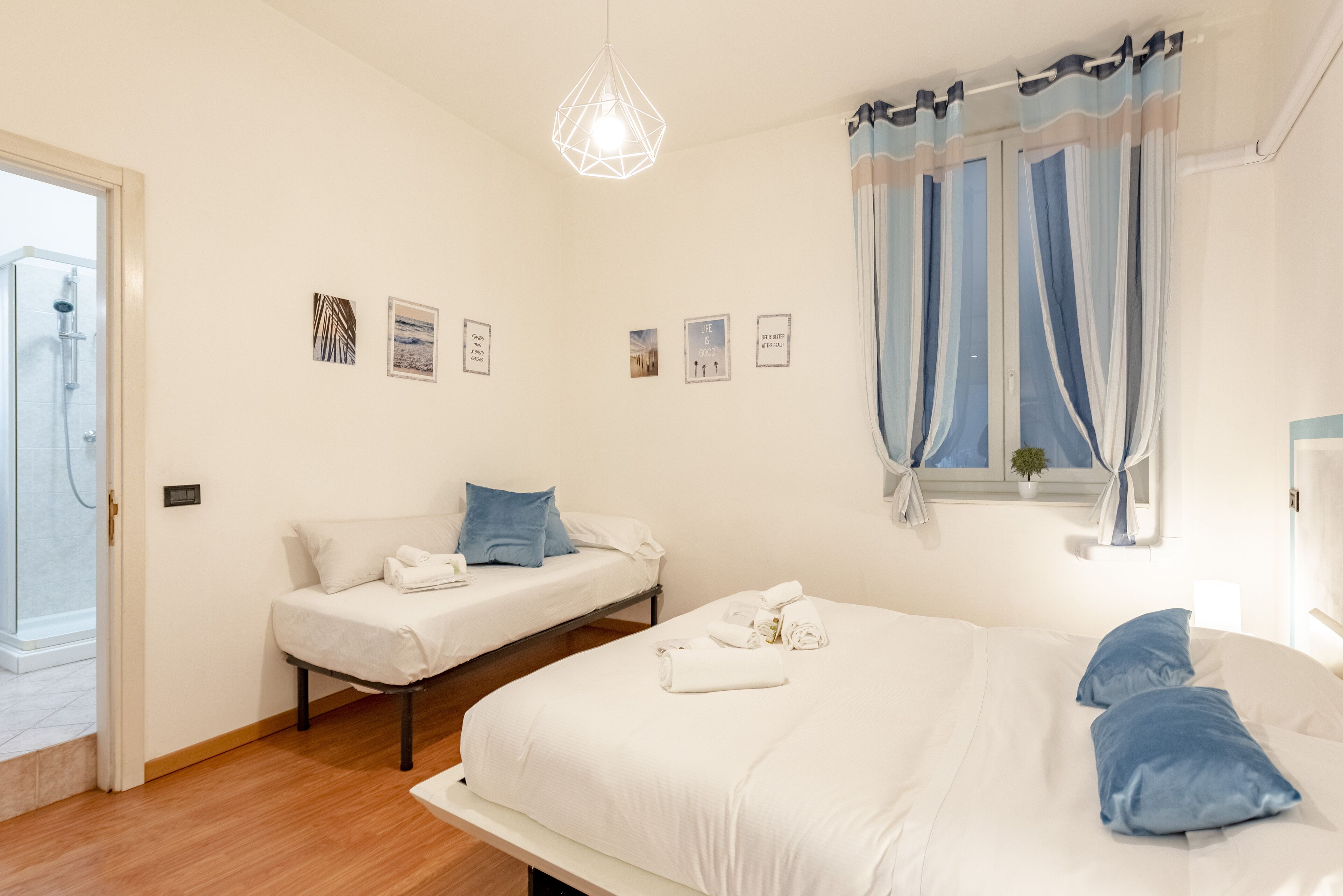 Ett hotellrum med en stor säng, två mindre sängar, en dusch och ett fönster med gardiner.