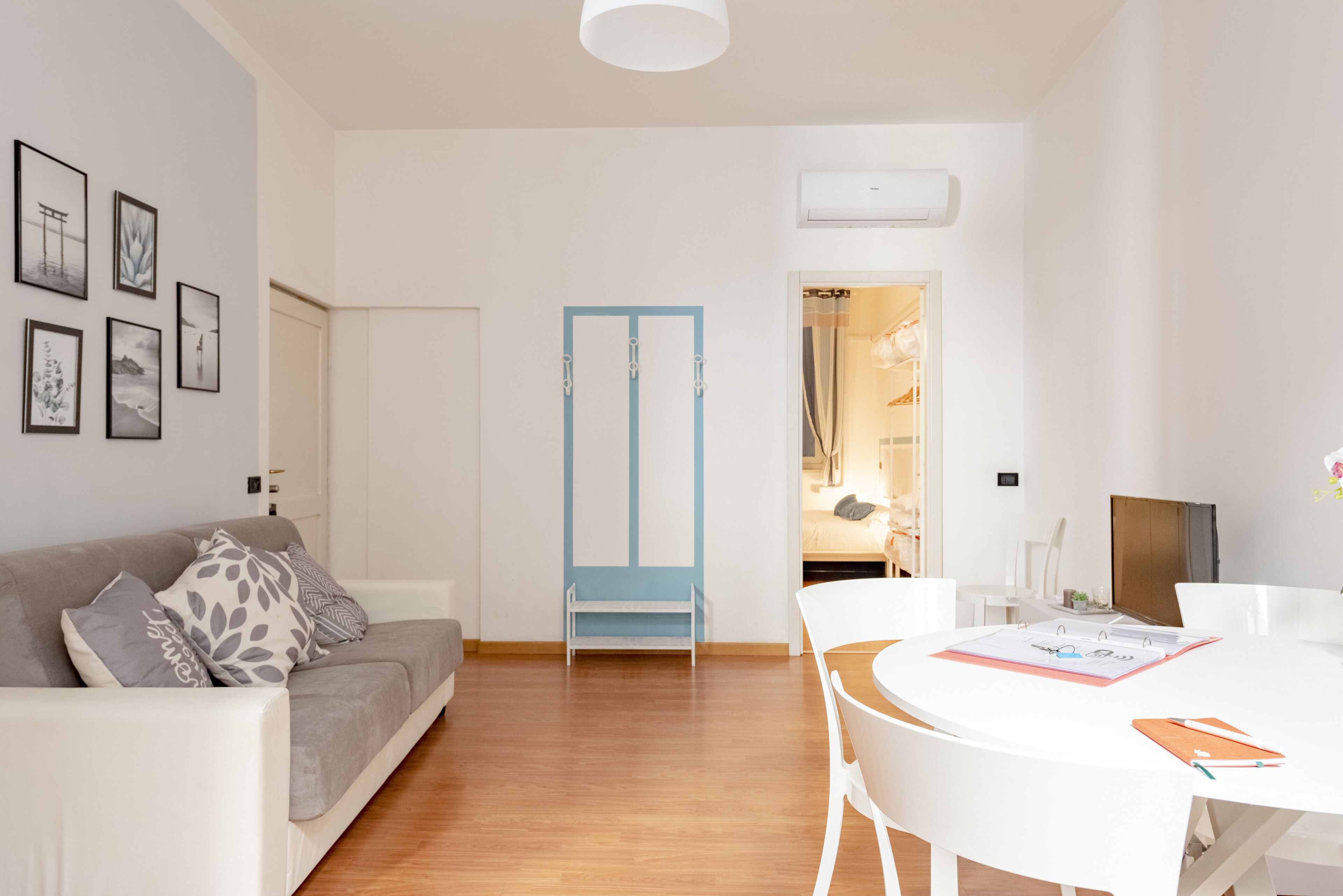 Una sala de estar moderna con un sofá gris, sillas blancas, una puerta azul y una mesa blanca con un cuaderno.