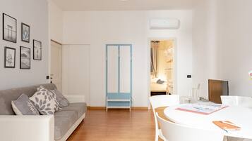 Una sala de estar moderna con un sofá gris, sillas blancas, una puerta azul y una mesa blanca con un cuaderno.
