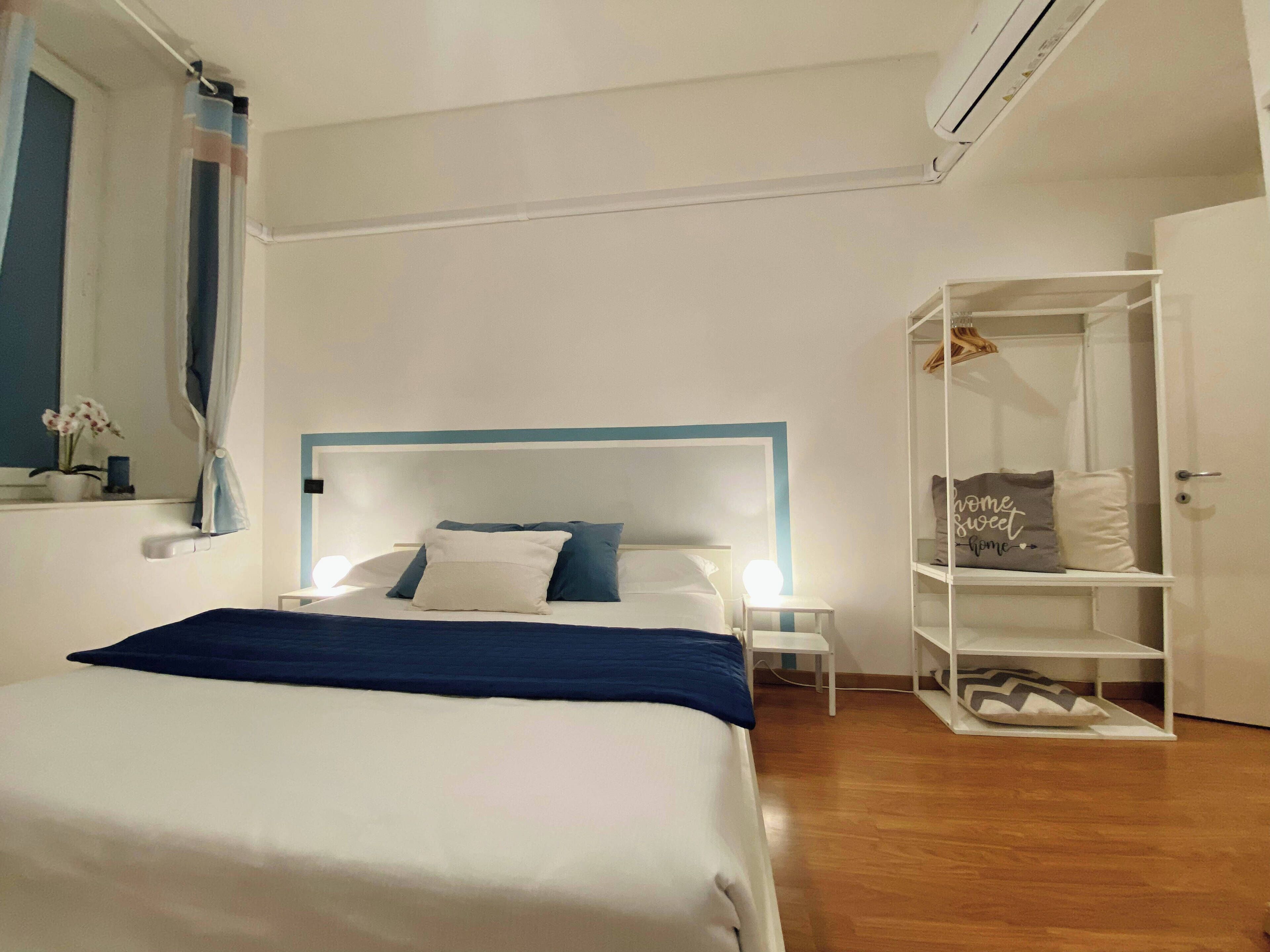 A bedroom with a bed, bedside tables, a wardrobe, and a shelf with items.