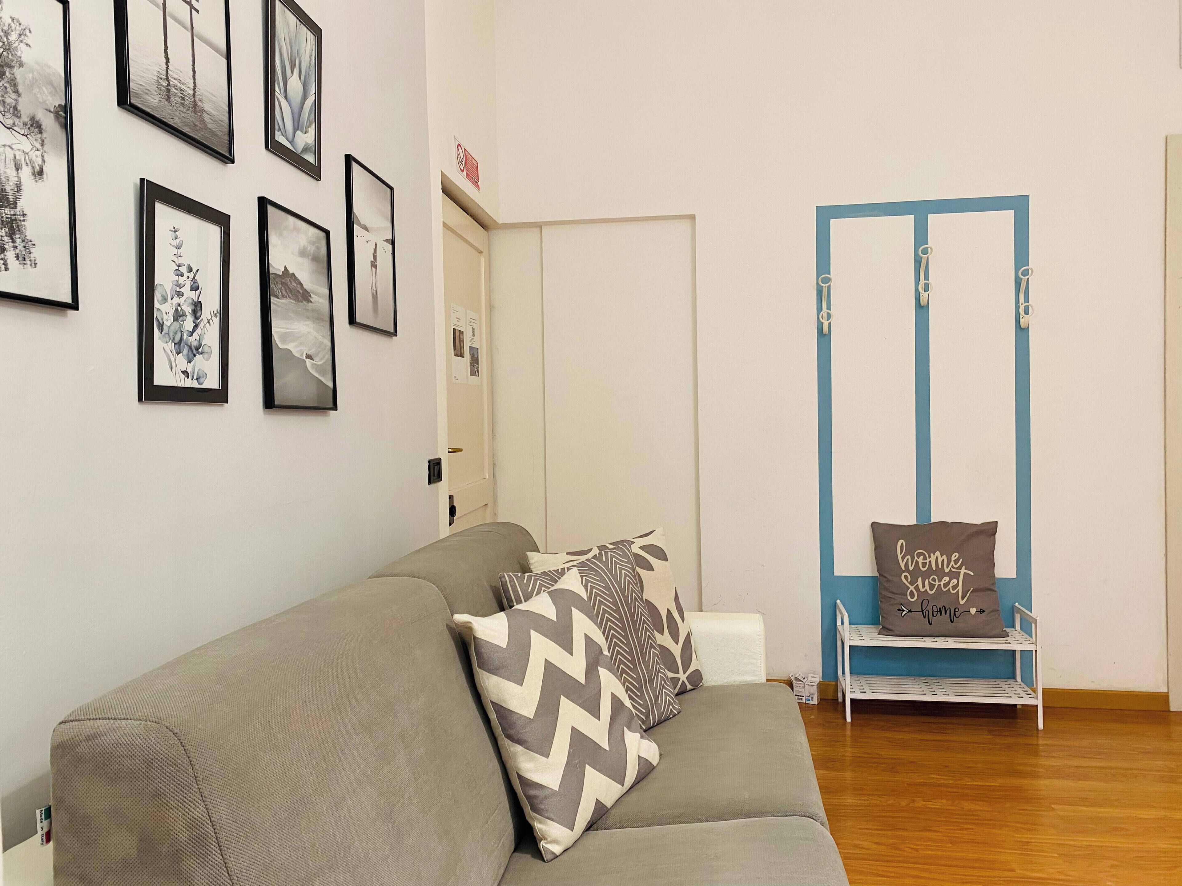 A living room with a grey sofa, a blue door, and a shelf with a cushion that says "home sweet home".