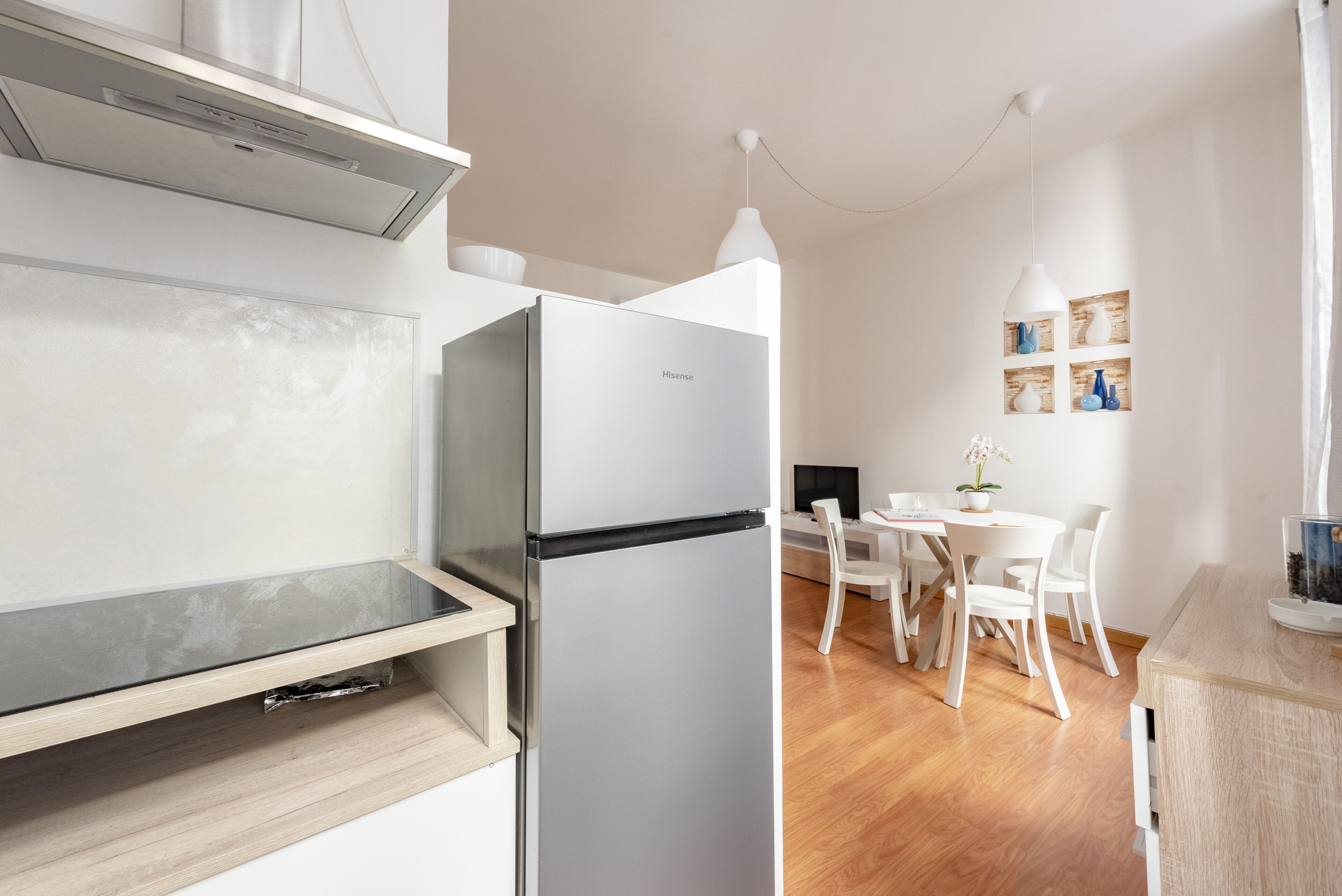 A modern kitchen with a built-in refrigerator, wooden cabinets, and a dining area with white chairs and a table.
