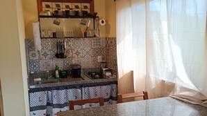 Une cuisine avec un mur recouvert de carreaux, un porte-ustensiles suspendu et une fenêtre ornée de rideaux légers.