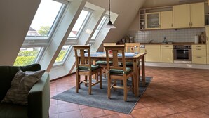 Un comedor con mesa y sillas, una cocina con armarios y electrodomésticos, y vistas a través de tragaluces.