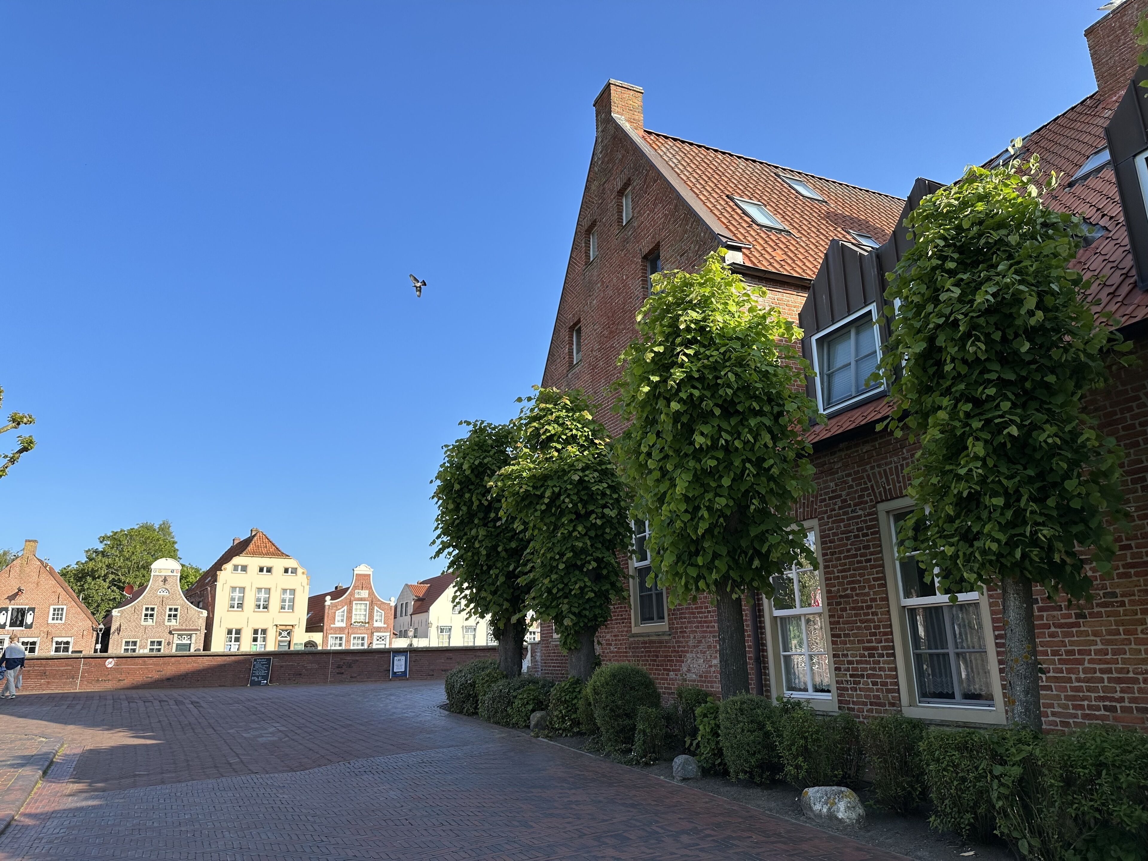 A traditional European street with brick buildings, a paved walkway, and a clear blue sky.