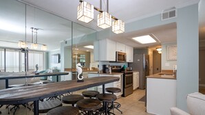 A modern kitchen with a central island, bar stools, and pendant lighting. - The Whaler D5 by Liquid Life (Gulf Shores)