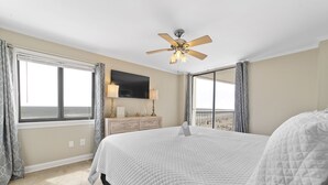 A bedroom with a large bed, a ceiling fan, a flat-screen TV, a dresser, and a window with curtains. - The Whaler D5 by Liquid Life (Gulf Shores)