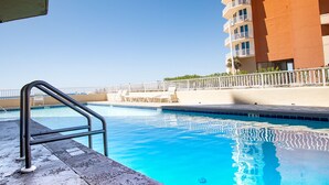 A swimming pool with a metal ladder, surrounded by a white fence and a building with balconies. - The Whaler D5 by Liquid Life (Gulf Shores)