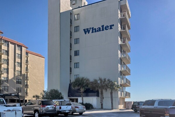 A Whaler hotel building with multiple floors, balconies, and parked vehicles in the foreground.