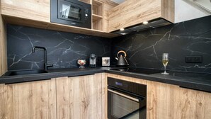 Een moderne keuken met houten kastjes, een zwart aanrecht, een ingebouwde magnetron, een waterkoker en een wijnglas.