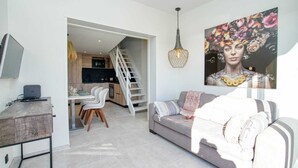 Een moderne woonkamer met een grijze bank, een eethoek met een witte tafel en stoelen, en een trap die leidt naar een verdieping.