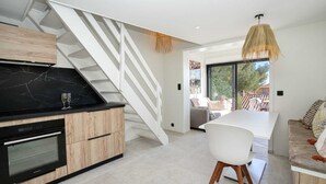 Een moderne keuken met een zwart marmeren aanrechtblad, houten kastjes en een ingebouwde oven. Een witte trap leidt naar een balkon met een hanglamp.