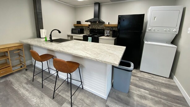 A compact kitchen with a central island, bar stools, a black refrigerator, and a microwave. - 2 bedroom Budget Suite. Open floor plan (Mattoon)