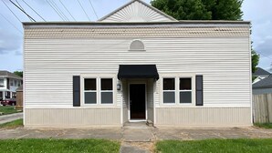 A single-story building with a front door, two windows with shutters, and a small overhang above the door. - 2 bedroom Budget Suite. Open floor plan (Mattoon)