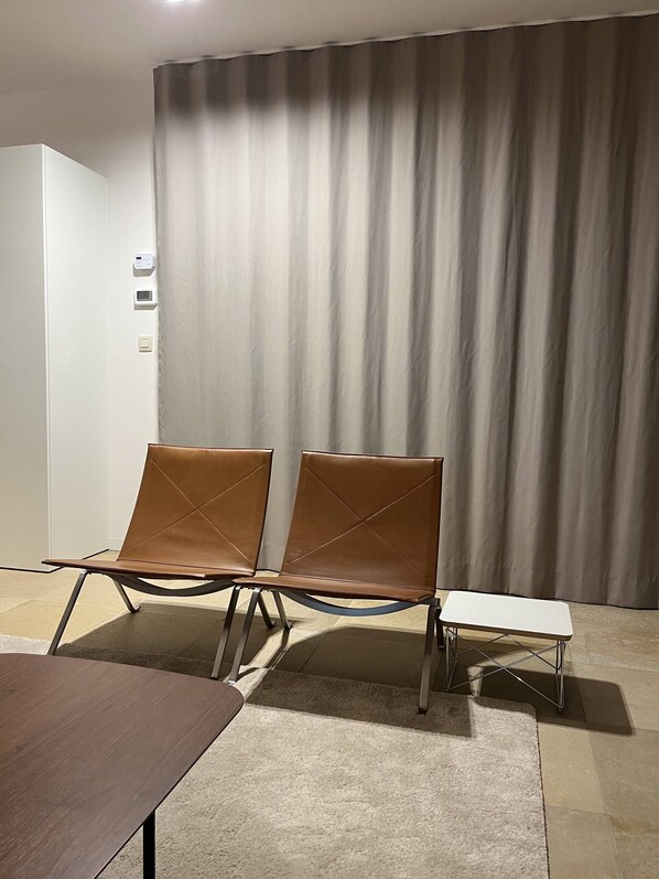 Habitació moderna amb dues butaques de pell, una taula petita blanca i un cortinó gran.
