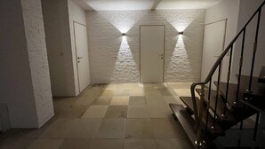 Un couloir avec un mur en briques blanches, une porte et un escalier.