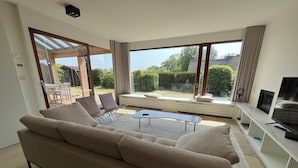 Un salon moderne avec un canapé beige, une table basse et un téléviseur posé sur un meuble de télévision blanc.