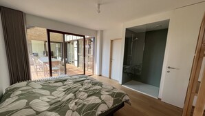 Une chambre à coucher comprenant un lit, une porte-fenêtre coulissante donnant sur une terrasse extérieure et un dressing.